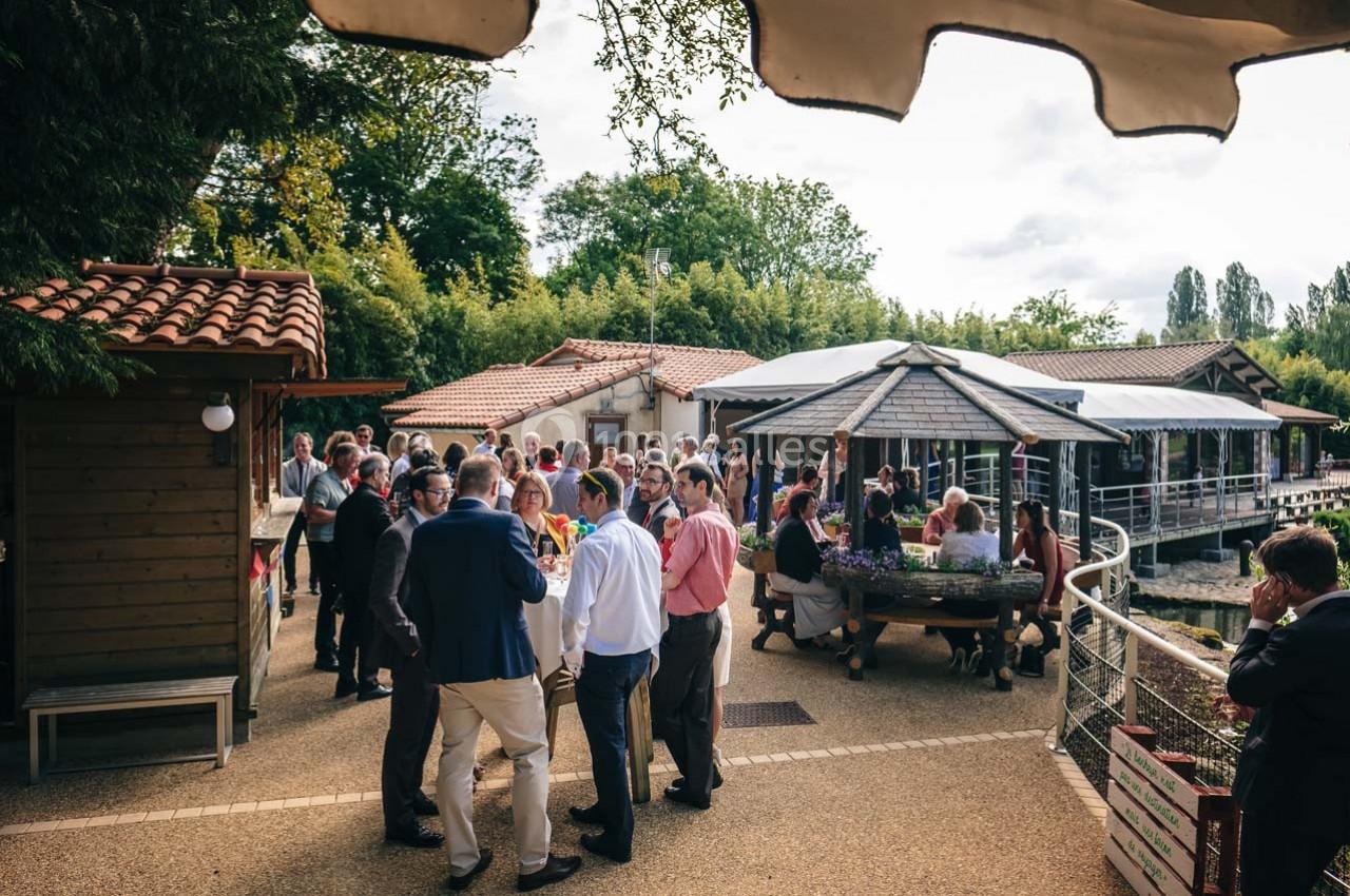 Groupe de personnes réunies en extérieur près de bâtiments et d'une terrasse couverte, dans un cadre verdoyant.