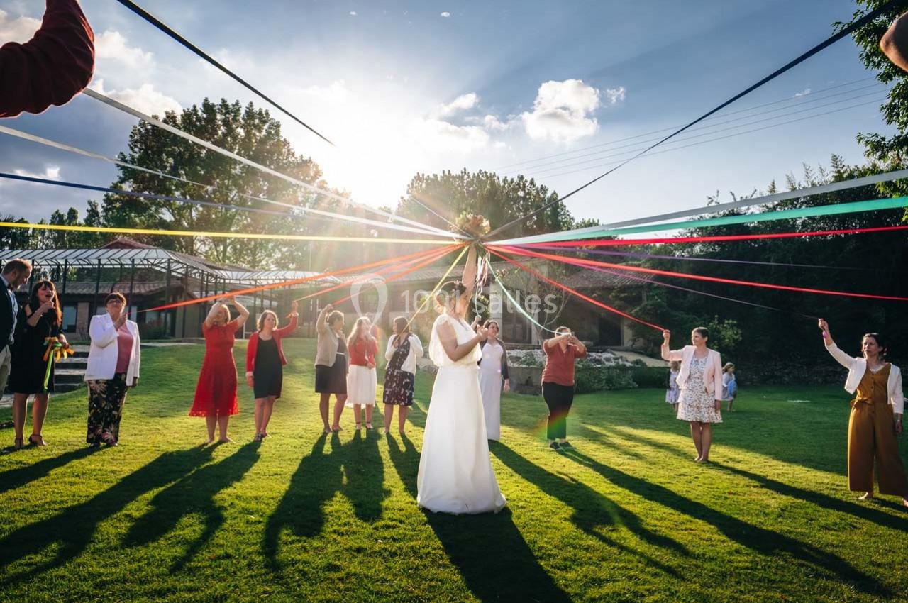 Des personnes dansent autour d'un mât décoré de rubans colorés sur une pelouse ensoleillée.