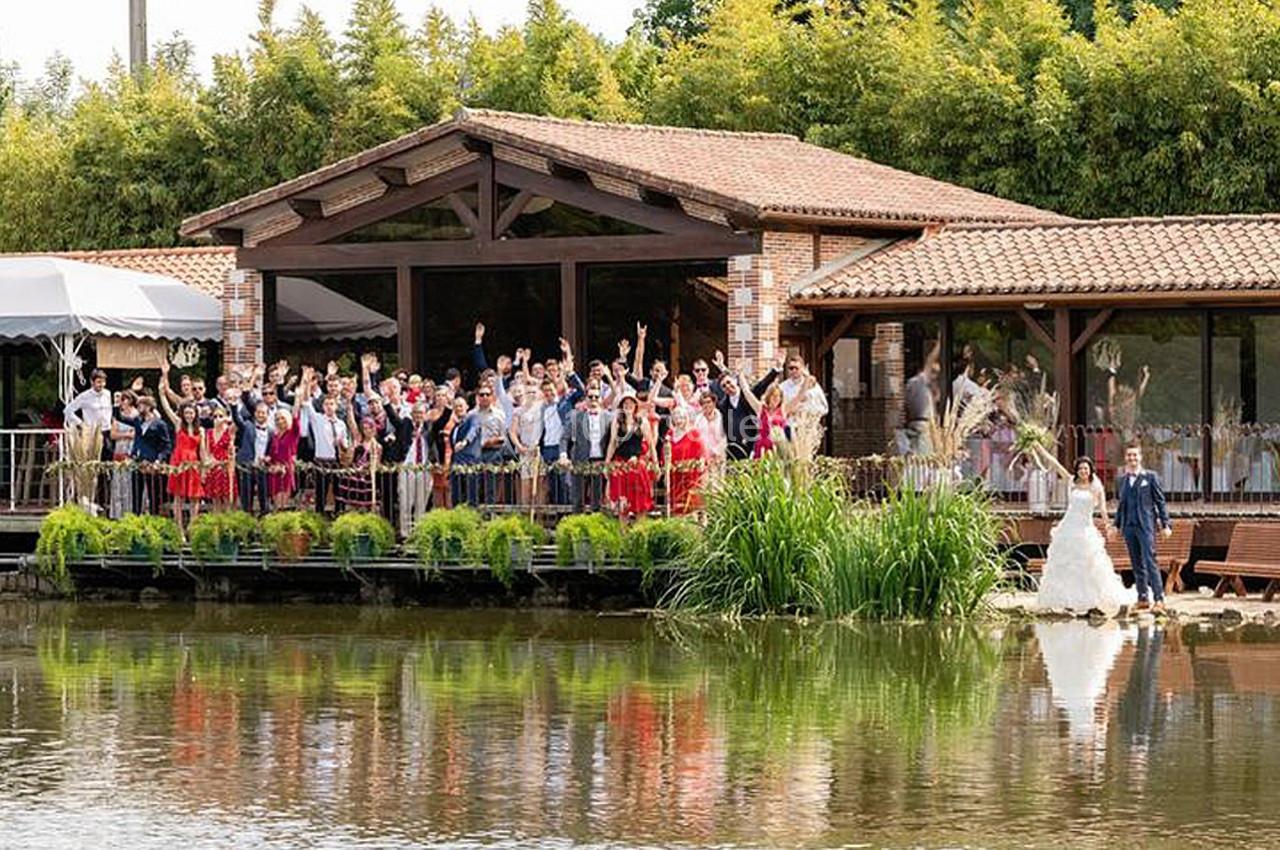 Un groupe de personnes pose devant un bâtiment en bois près d'un étang, avec des plantes et des arbres en arrière-plan.