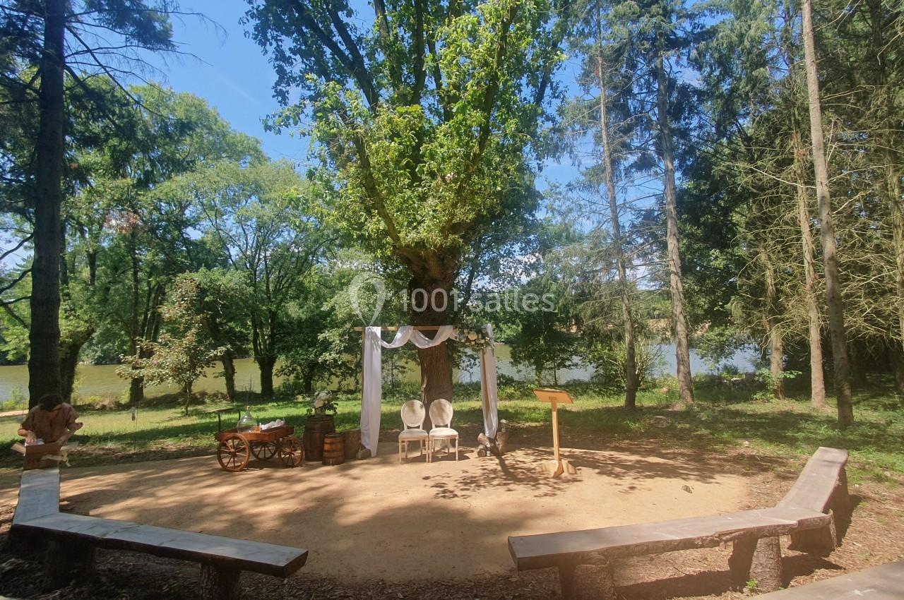 Espace extérieur aménagé pour une cérémonie, avec une arche décorée sous un grand arbre près d'un étang.