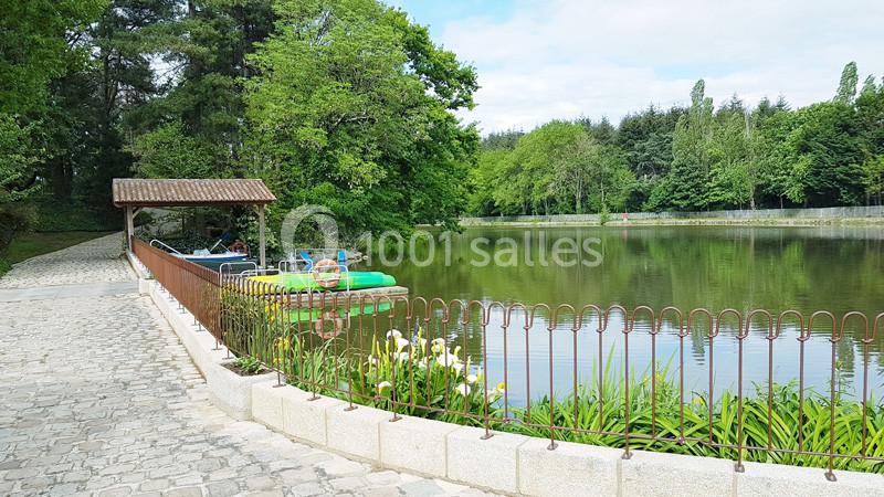 Chemin pavé longeant un étang bordé de végétation, avec des pédalos amarrés sous un abri en bois.