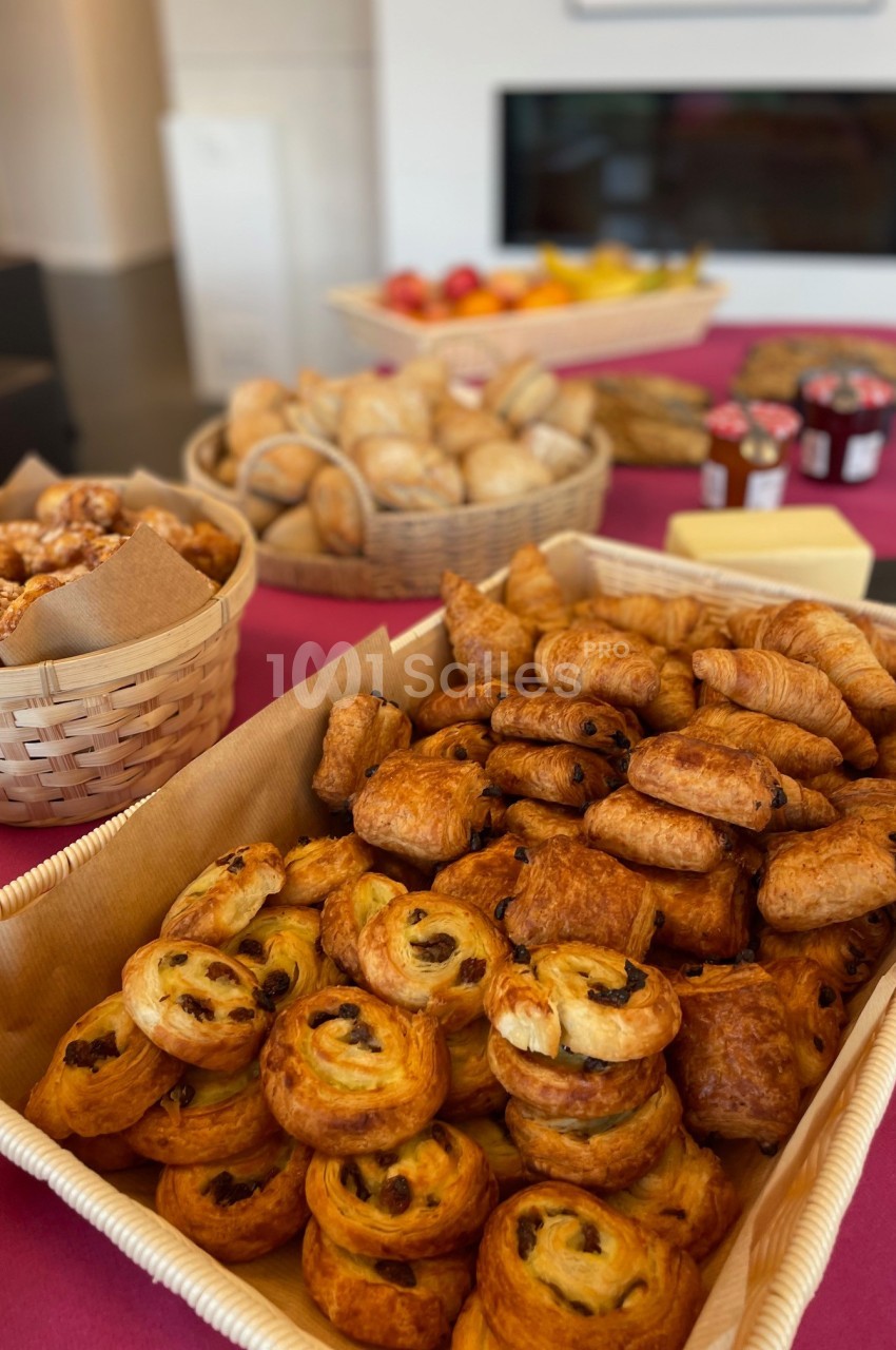 Plateau de viennoiseries variées avec croissants, pains aux raisins et autres, disposé sur une table rouge.