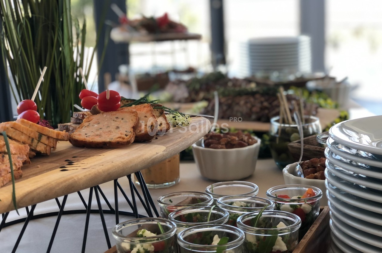 Buffet avec des plats variés, incluant des verrines, du pain, des légumes et des assiettes empilées en arrière-plan.