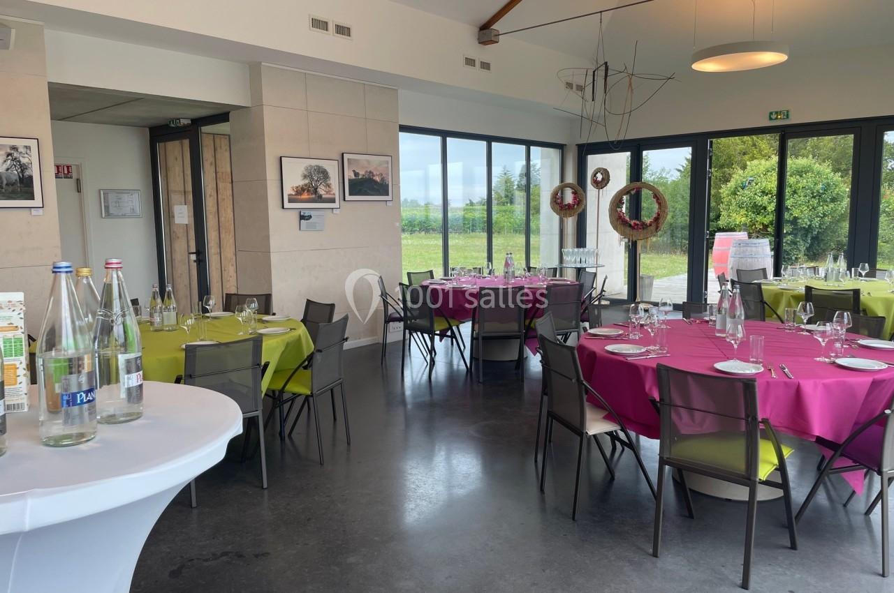 Salle de restaurant lumineuse avec tables dressées, nappes colorées et grandes baies vitrées donnant sur un espace vert.