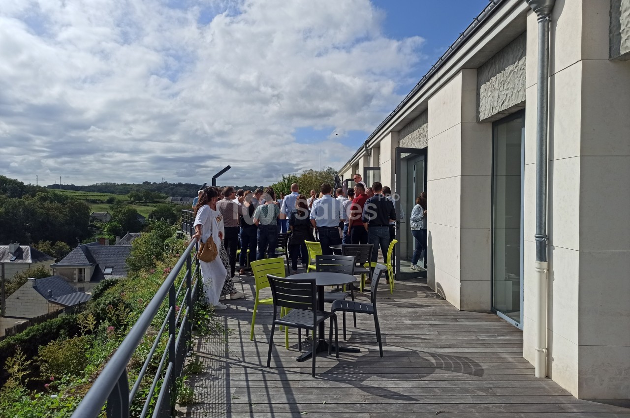 Un groupe de personnes discute sur une terrasse ensoleillée avec vue sur un paysage verdoyant.