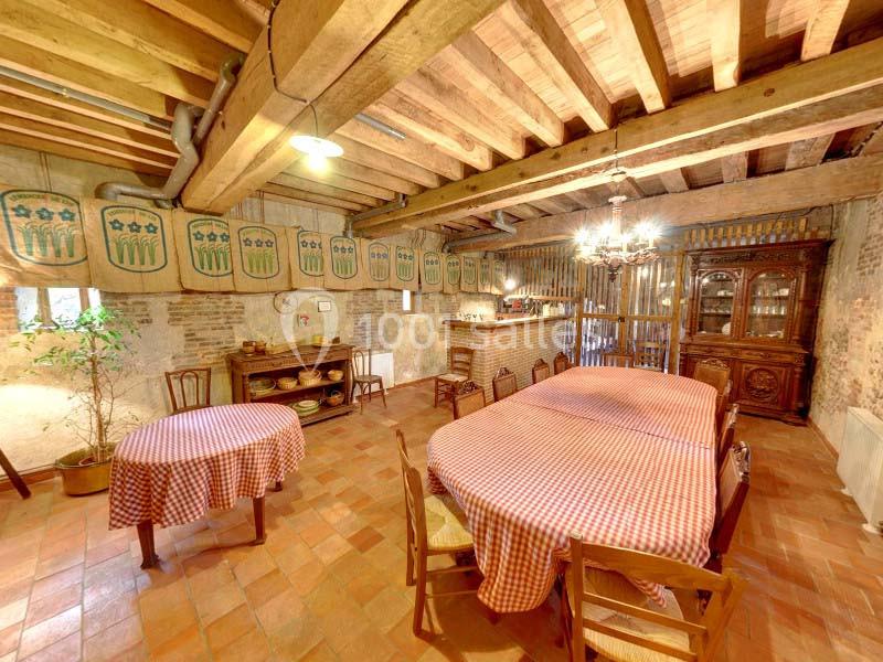 Salle à manger rustique avec poutres apparentes, tables couvertes de nappes à carreaux rouges et mobilier en bois.