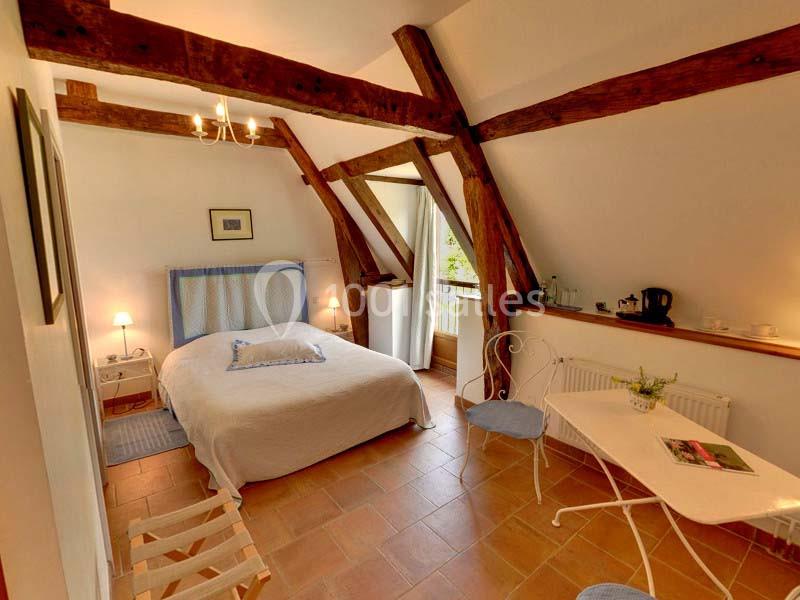 Chambre lumineuse avec poutres apparentes, lit double, table blanche, et vue sur un balcon avec verdure.