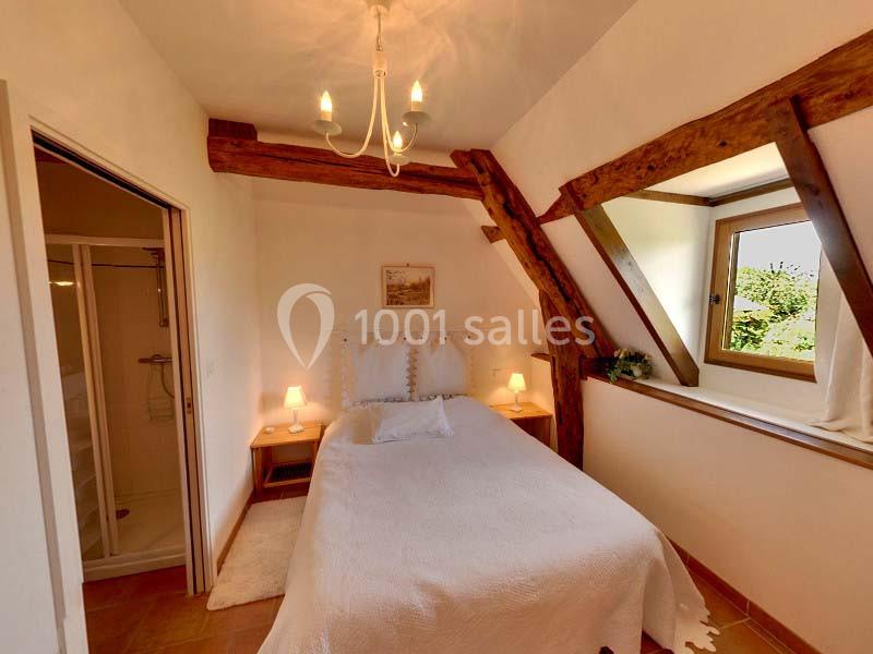 Chambre lumineuse avec lit simple, poutres apparentes, fenêtre donnant sur l'extérieur et salle de bain attenante.