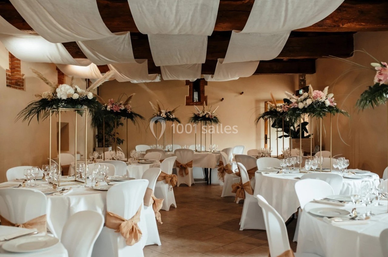Salle de réception décorée avec des tables rondes, nappes blanches, chaises ornées et compositions florales élégantes.