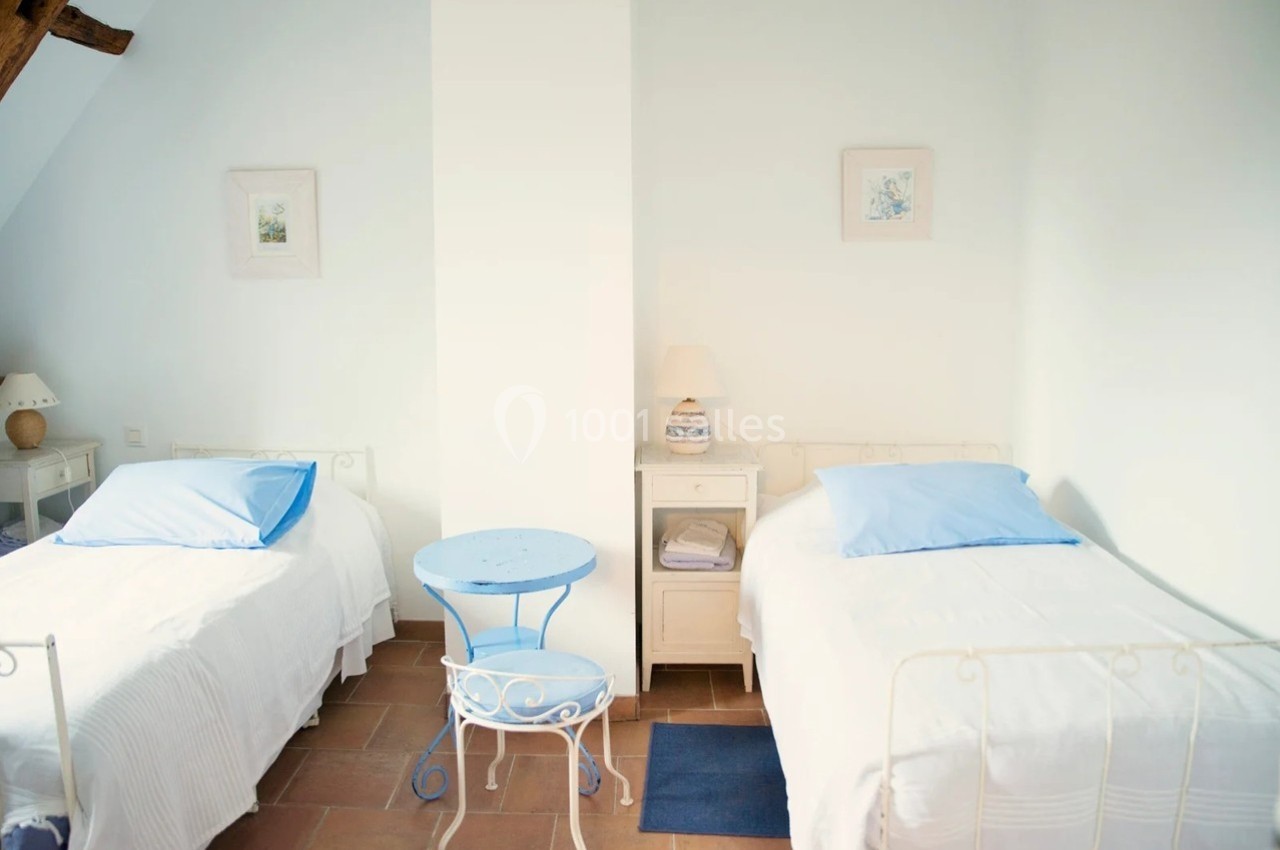 Deux lits simples avec draps blancs et oreillers bleus, une table bleue et des lampes sur des tables de chevet dans une…