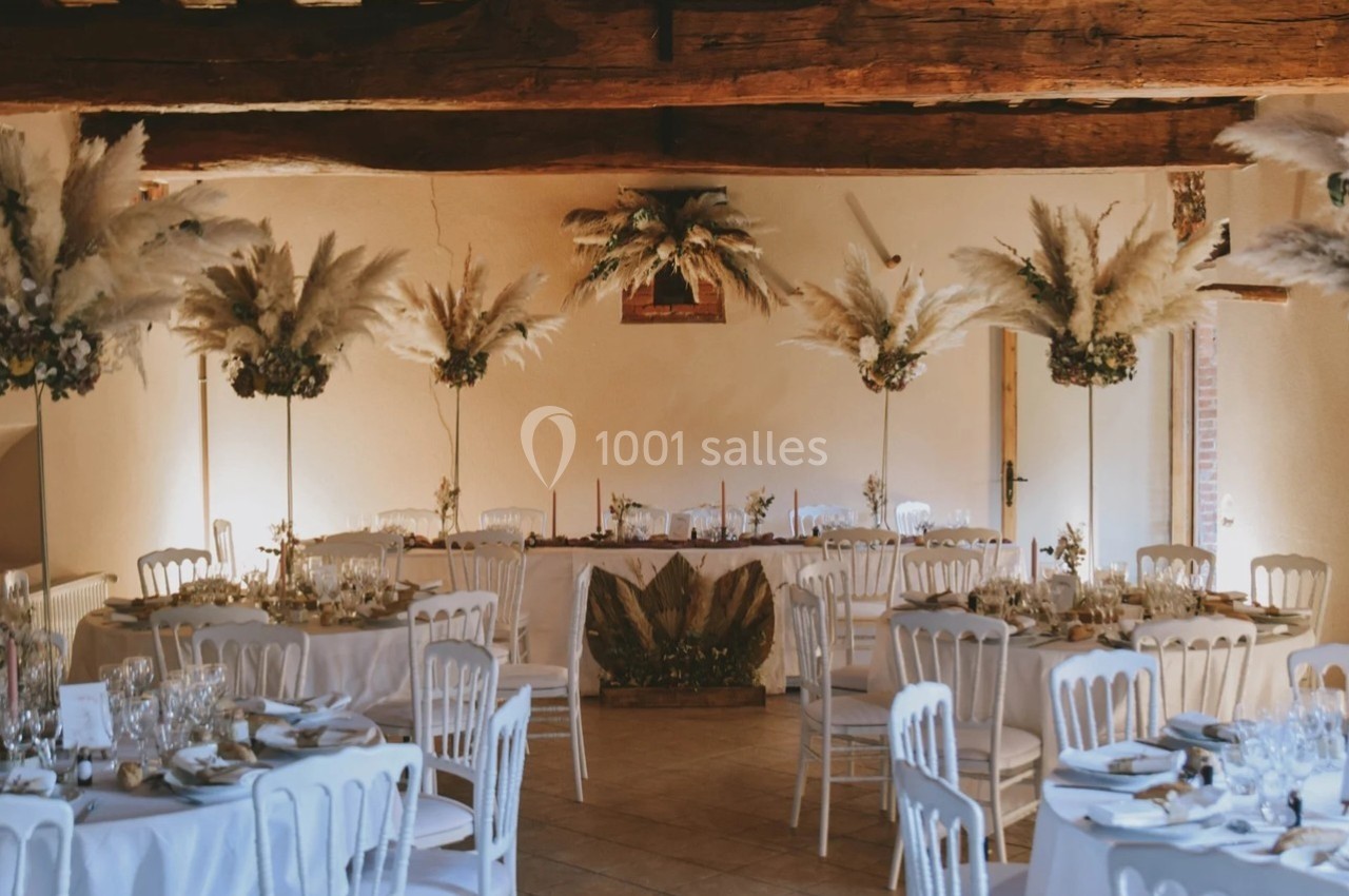 Salle de réception décorée avec des tables rondes, nappes blanches, chaises assorties et compositions de pampas.