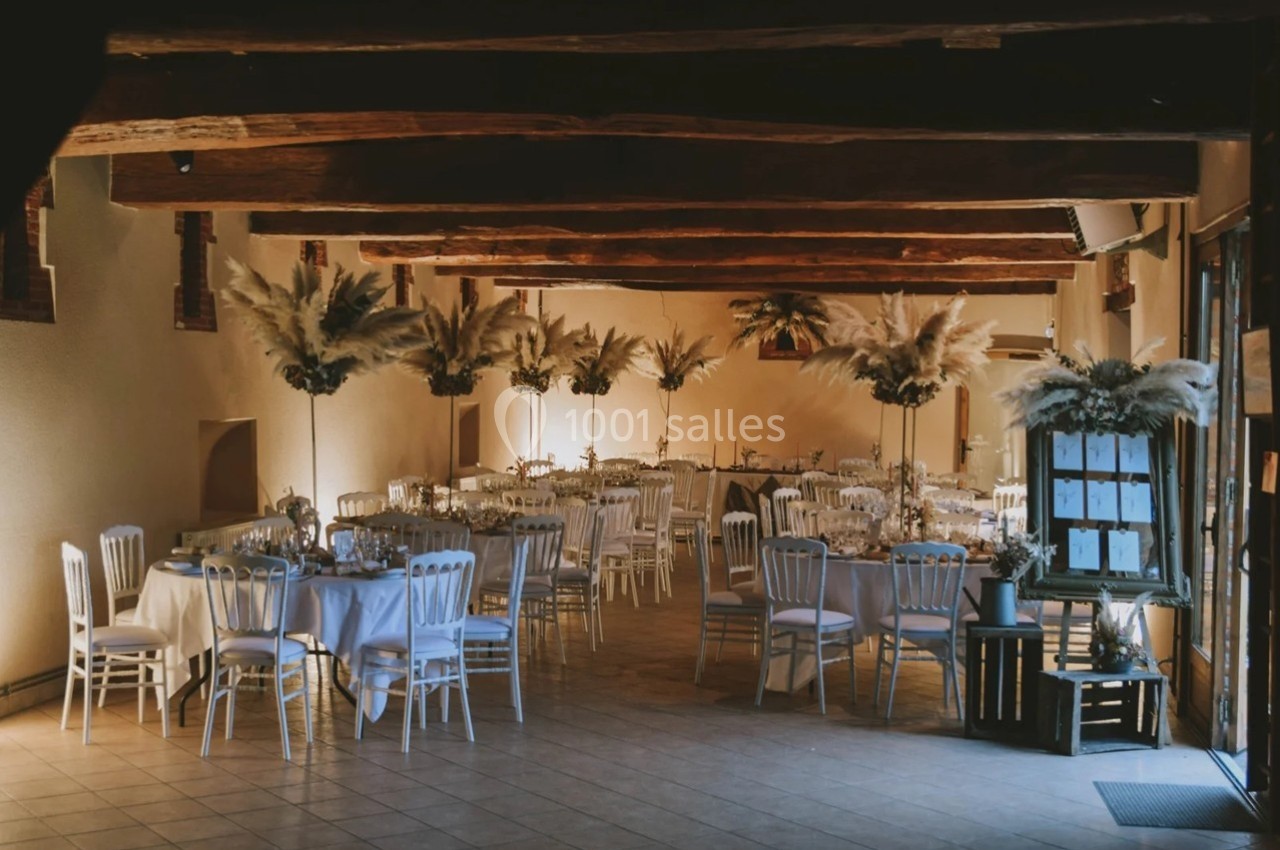 Salle de réception décorée avec des tables rondes, chaises blanches et arrangements floraux à base de pampas.