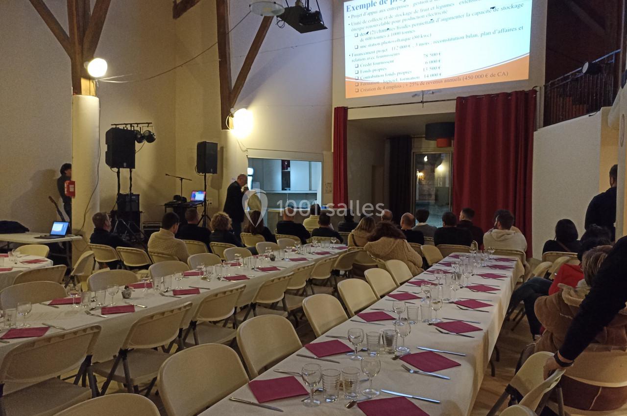 Salle de conférence avec des tables dressées et des participants écoutant une présentation projetée sur un écran.
