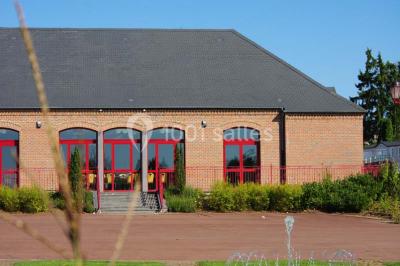 Salle de réunion vide avec tables disposées en U, chaises en bois, murs en briques et grandes fenêtres laissant entrer la…