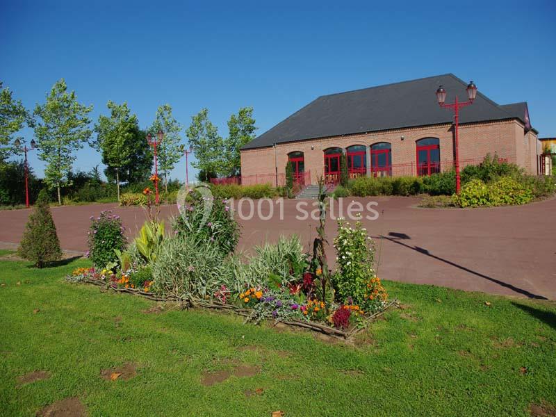 Bâtiment en briques rouges avec toit en ardoise, entouré d'un parterre fleuri et d'une place dégagée.