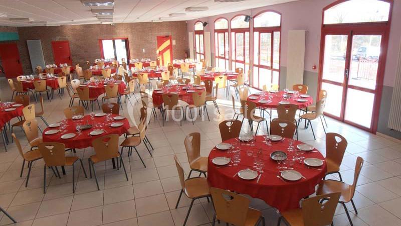 Salle de réception lumineuse avec des tables rondes dressées de nappes rouges et chaises en bois clair.