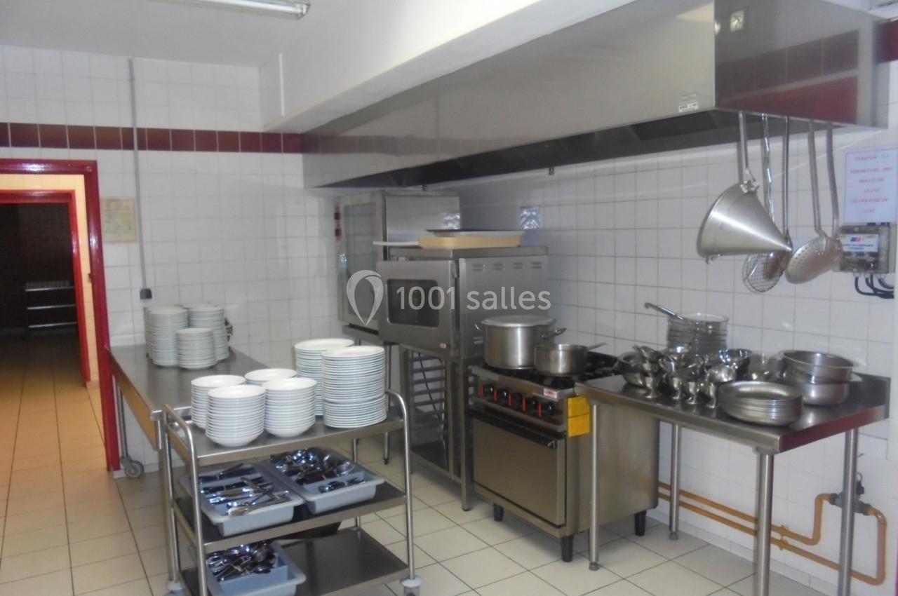 Cuisine professionnelle équipée avec four, plaques de cuisson, ustensiles suspendus et chariots contenant assiettes et…