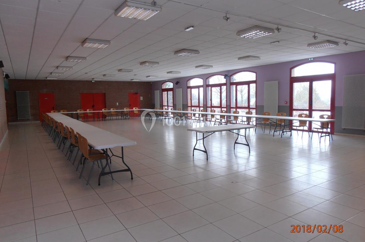 Salle spacieuse avec tables et chaises alignées, grandes fenêtres laissant entrer la lumière naturelle.