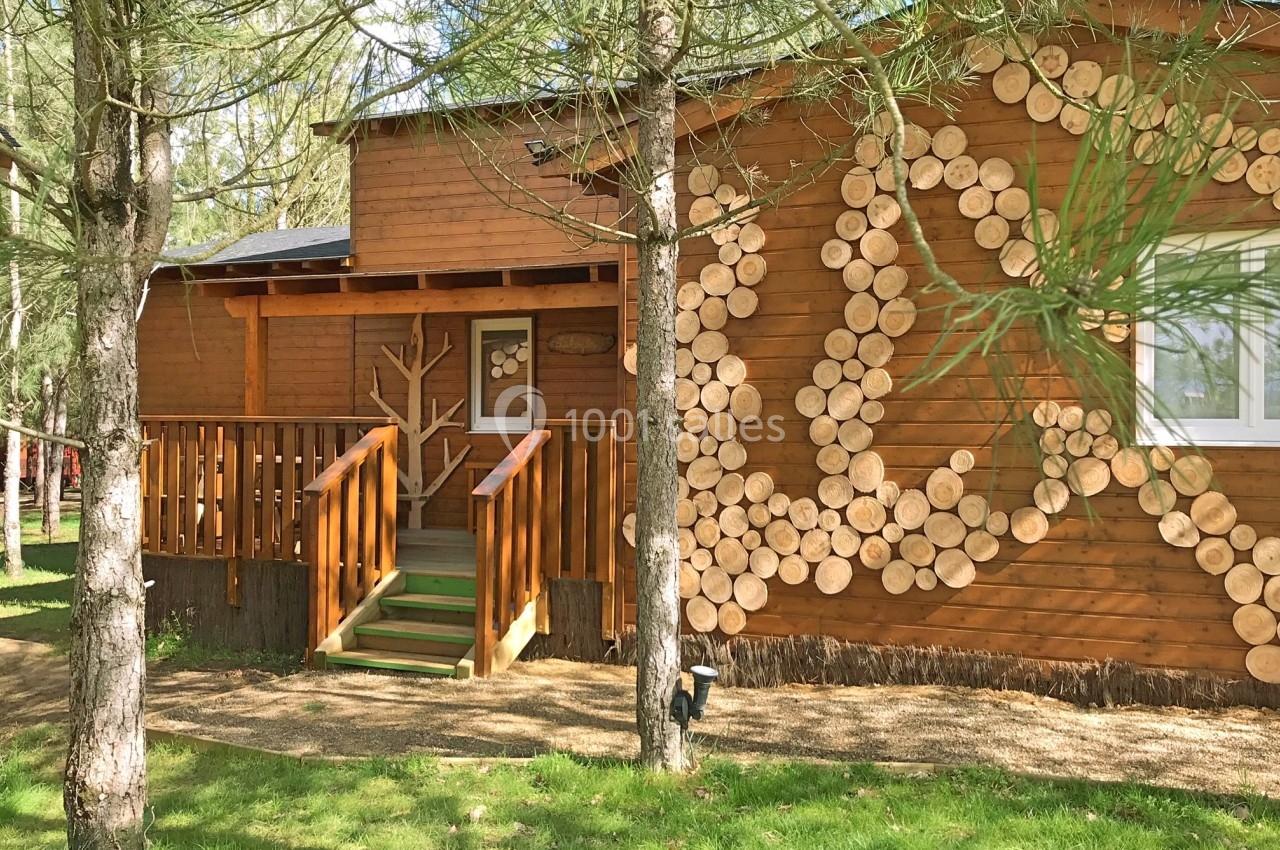 Chalet en bois décoré de rondins, entouré d'arbres, avec une petite terrasse et un escalier en bois.