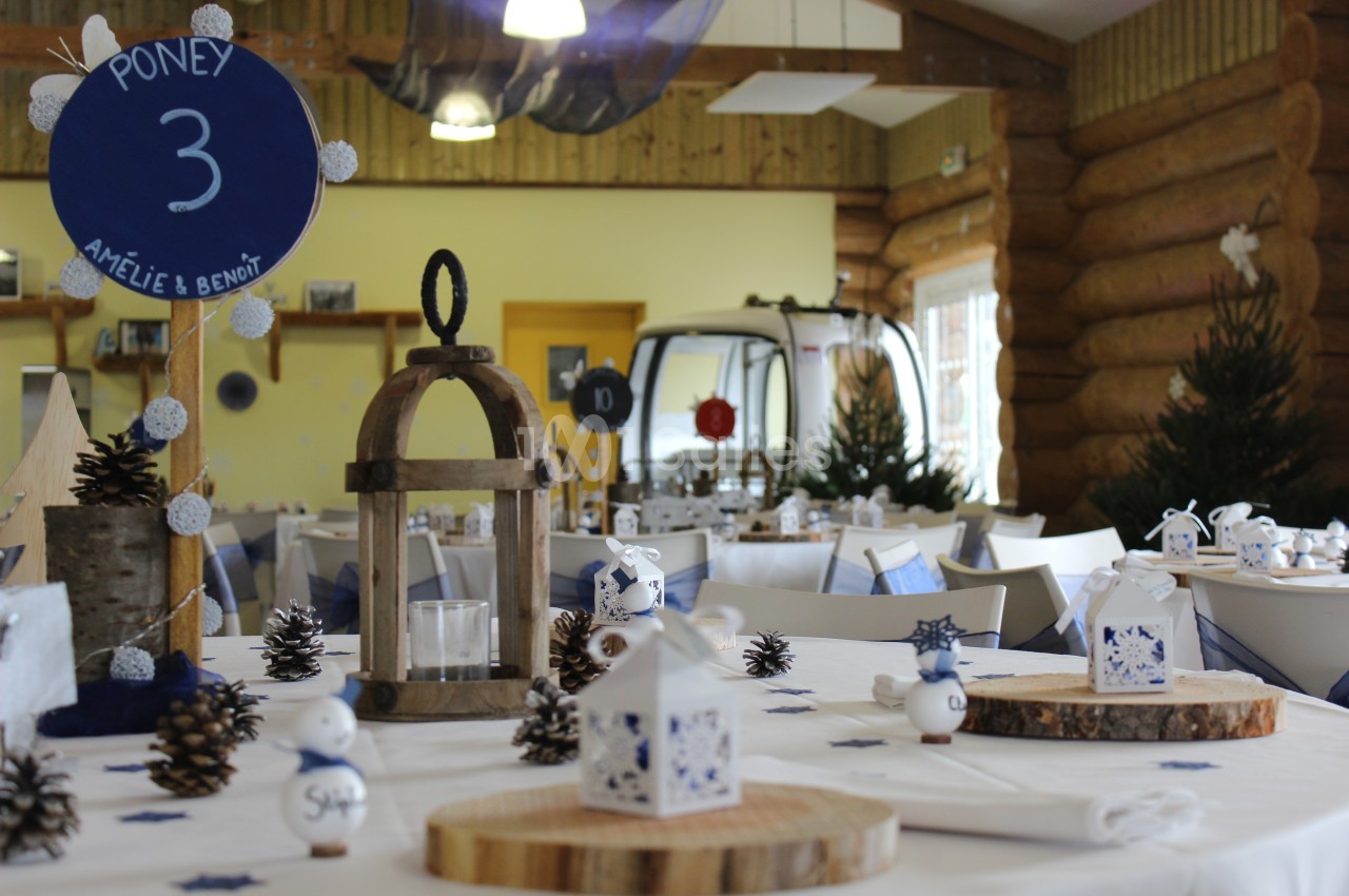Salle décorée pour un événement avec des tables dressées, des lanternes en bois, des rondins et des éléments hivernaux.