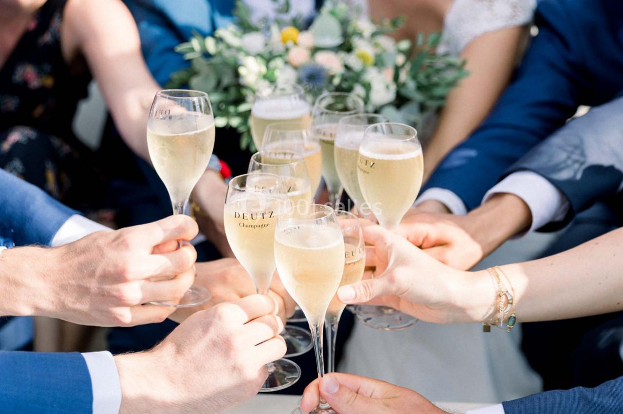 Des mains trinquent avec des coupes de champagne devant un bouquet de fleurs.