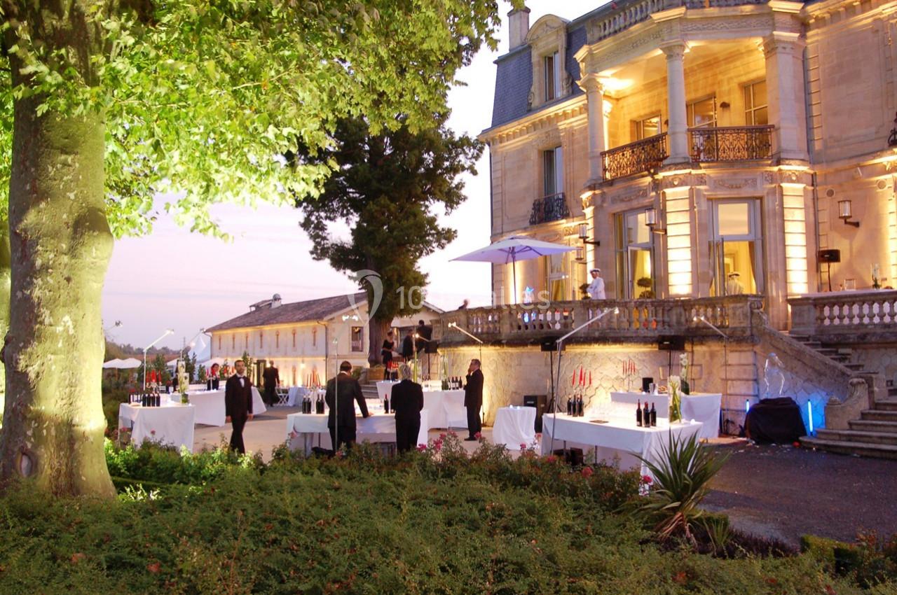 Réception en plein air au crépuscule devant un bâtiment historique éclairé, avec tables dressées et invités debout.