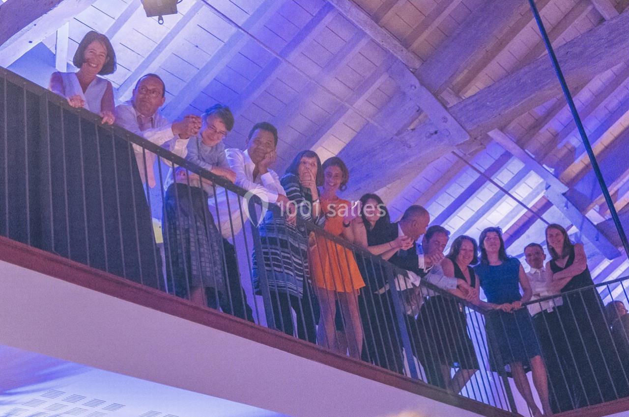 Un groupe de personnes se tient sur une mezzanine en bois sous un plafond éclairé de lumières bleutées.