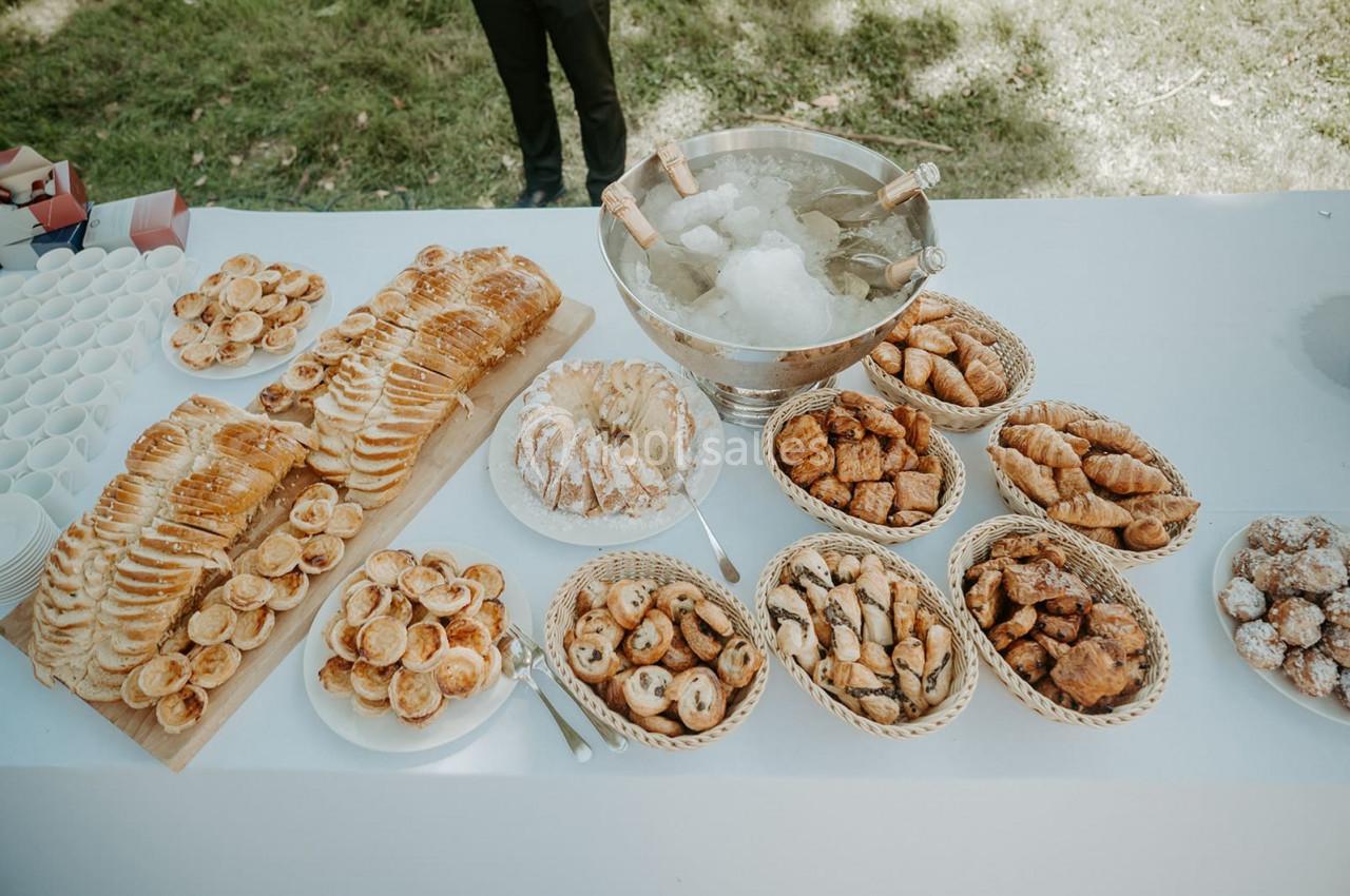 Table garnie de viennoiseries, pâtisseries et pain, avec un seau à glace au centre, en extérieur.
