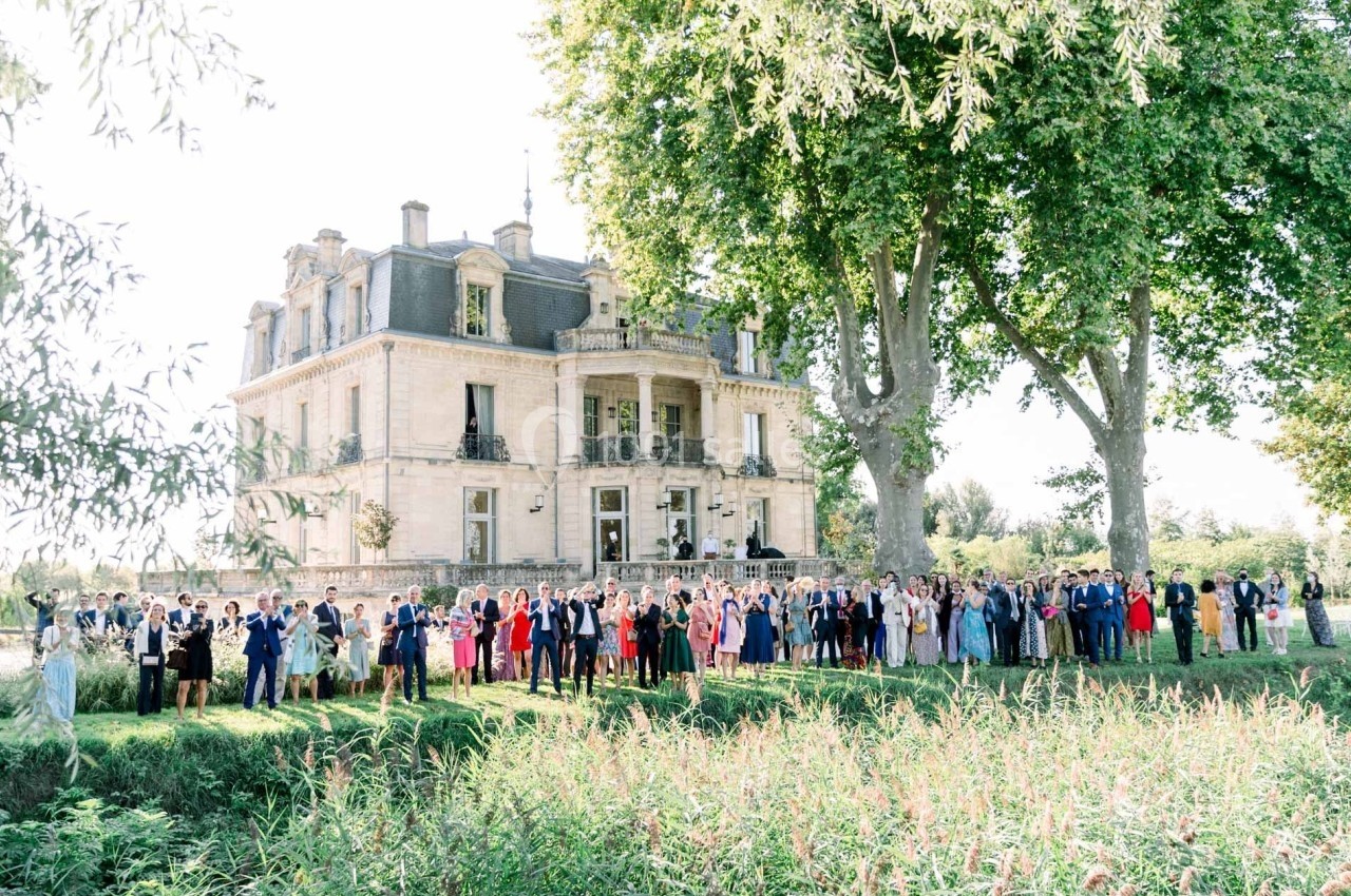 Groupe de personnes posant devant un grand château entouré de verdure par une journée ensoleillée.