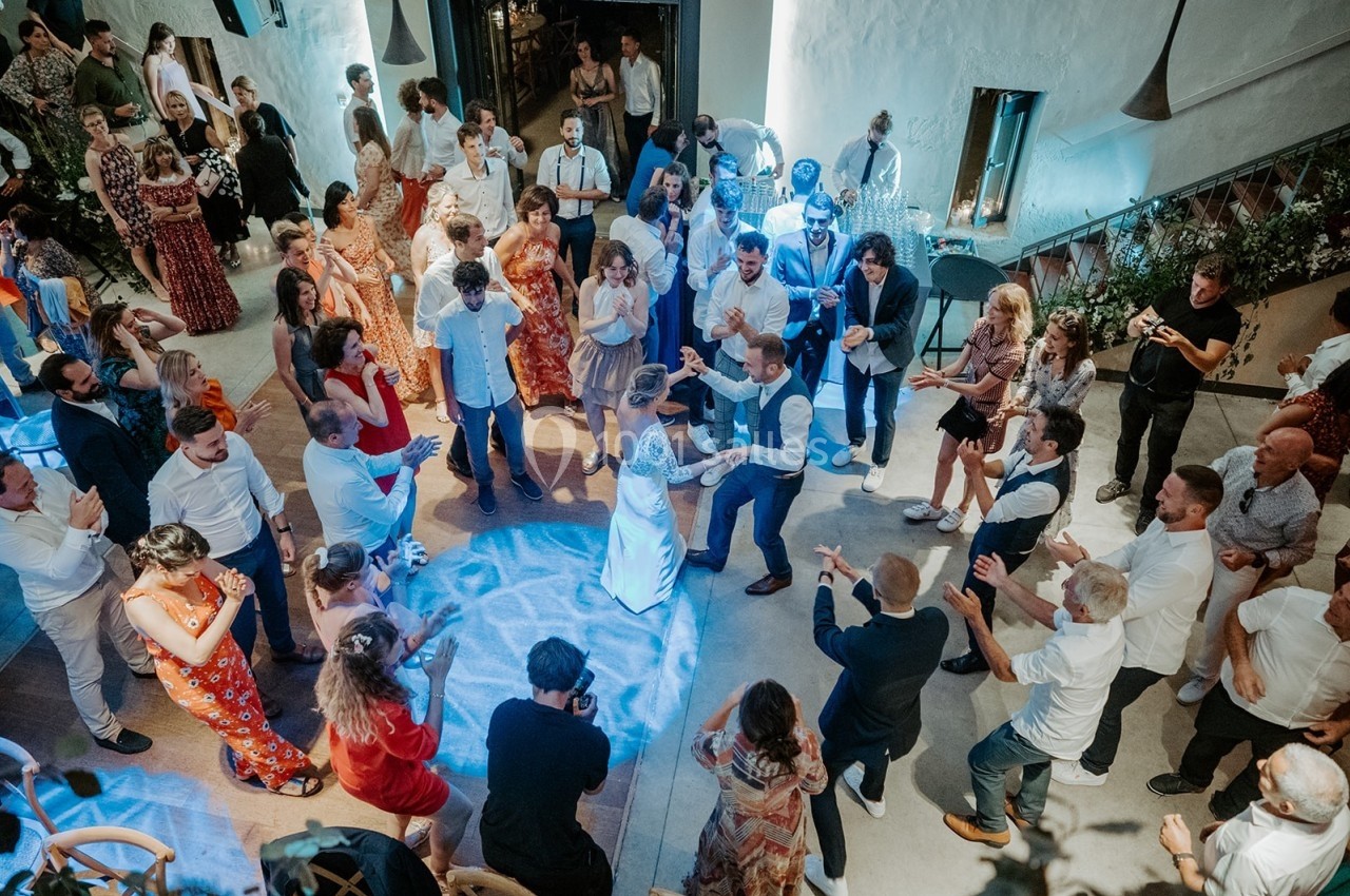 Groupe de personnes dansant lors d'une fête ou d'un mariage, dans une salle lumineuse avec une ambiance festive.