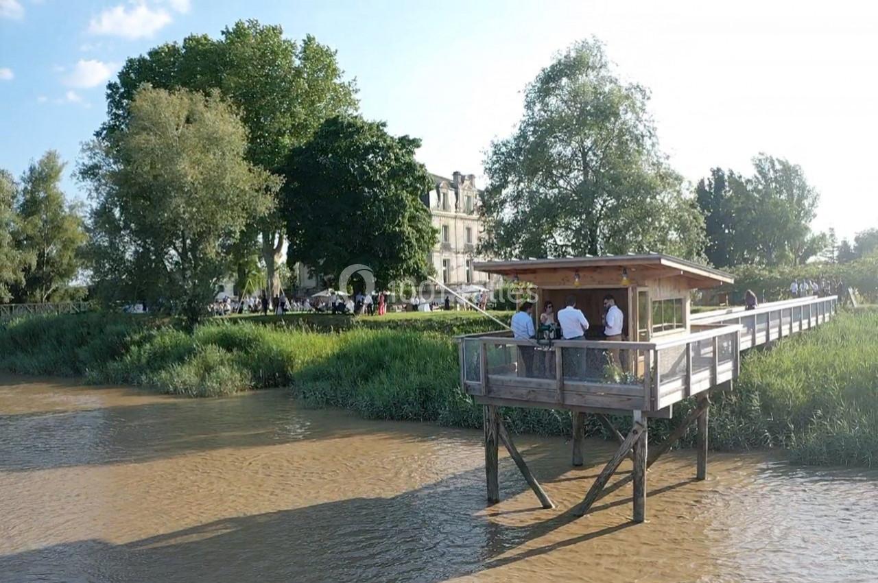 Un ponton en bois surplombant une rivière, entouré de verdure et d'arbres, avec des personnes rassemblées dessus.