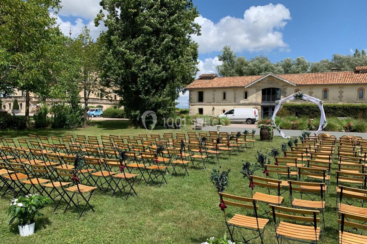 Chaises en bois disposées en rangées sur une pelouse pour une cérémonie en plein air, avec un arche décoré en arrière-plan.
