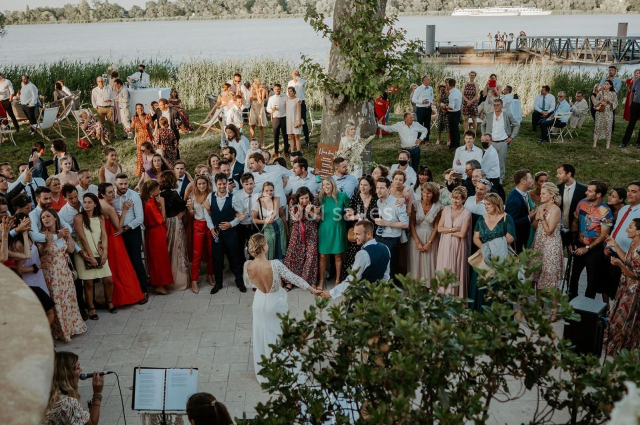Un groupe de personnes rassemblées en extérieur près d'un fleuve, lors d'un événement festif avec musiciens.