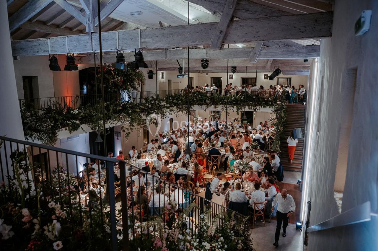 Salle de réception lumineuse avec de nombreuses tables dressées et des invités réunis pour un événement festif.