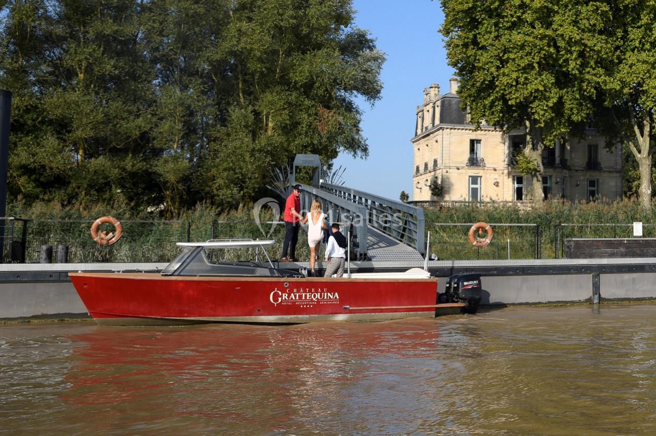 Un bateau rouge amarré près d'un quai, avec des passagers montant ou descendant, et un bâtiment en arrière-plan.