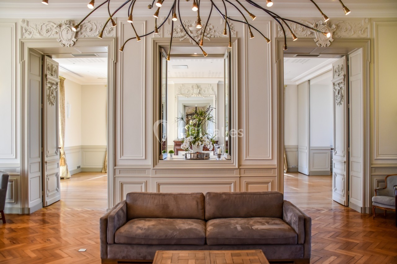 Salon élégant avec un canapé en velours marron, parquet en bois et miroirs encadrés dans un décor classique.