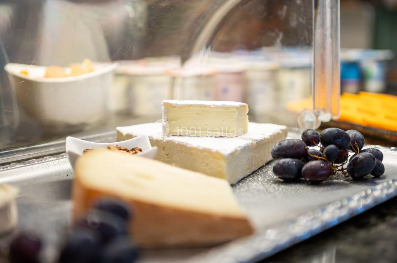 Plateau de fromages variés avec raisins noirs et noix, présenté sous une vitrine réfrigérée.