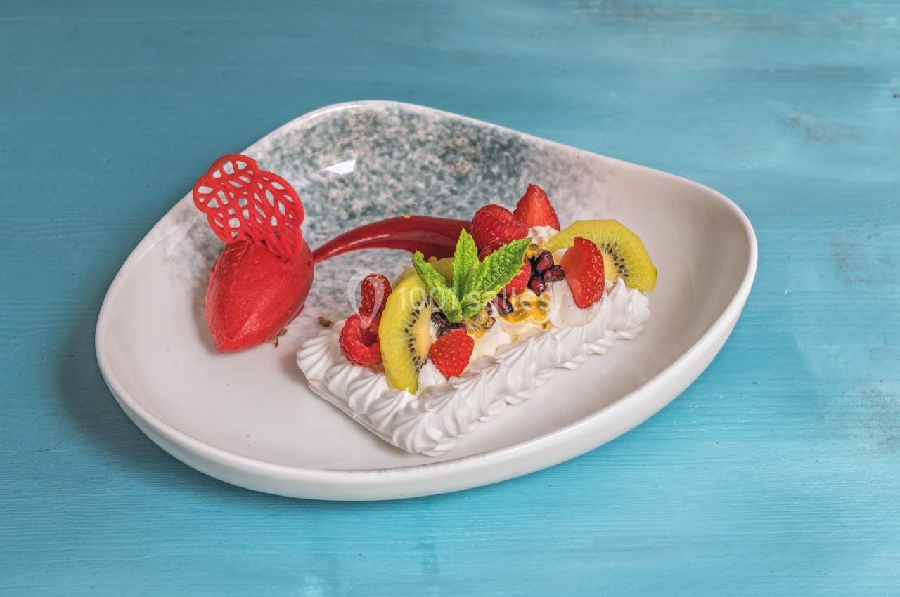 Dessert composé de meringue, fruits frais, sorbet rouge et décorations, présenté sur une assiette blanche.