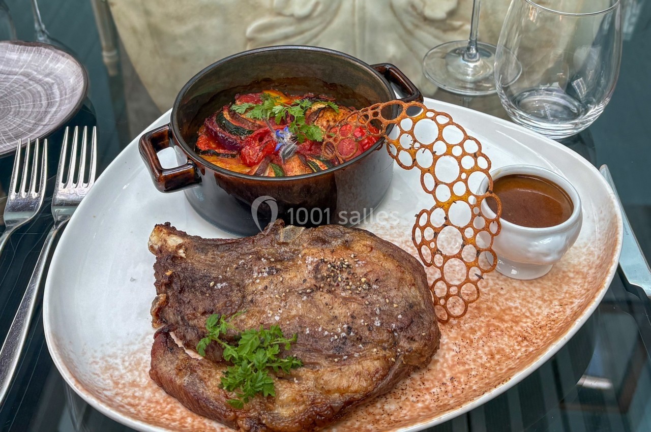 Côte de bœuf grillée servie avec ratatouille, sauce à part et décoration croustillante sur une assiette élégante.