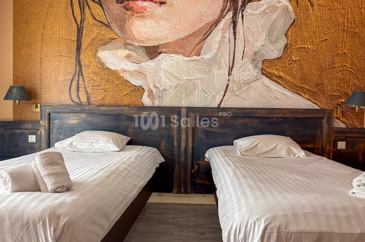 Deux lits simples avec draps blancs, appuyés contre un mur décoré d'une peinture murale artistique.