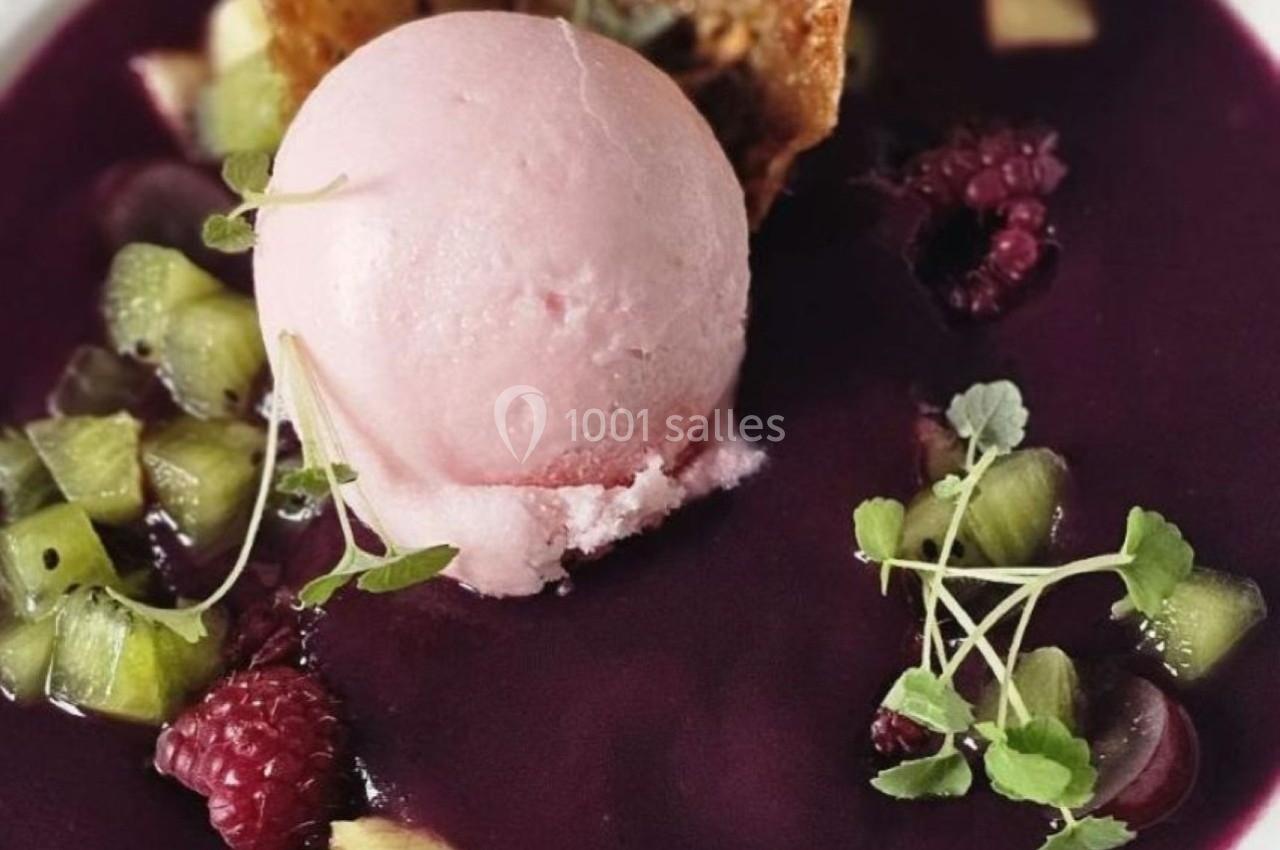 Assiette de soupe de fruits rouges avec une boule de glace rose, morceaux de kiwi, framboises et tuile croustillante.