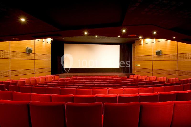 Salle de cinéma vide avec des rangées de fauteuils rouges et un grand écran blanc éclairé.