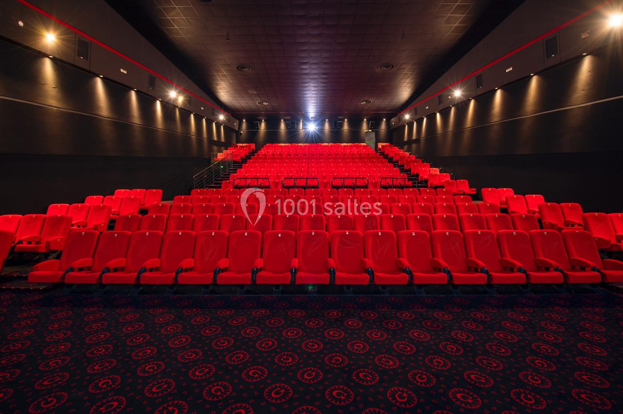 Salle de cinéma vide avec des rangées de sièges rouges et un éclairage tamisé.