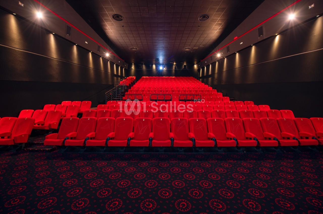 Salle de cinéma vide avec des rangées de sièges rouges et un sol recouvert de motifs circulaires.