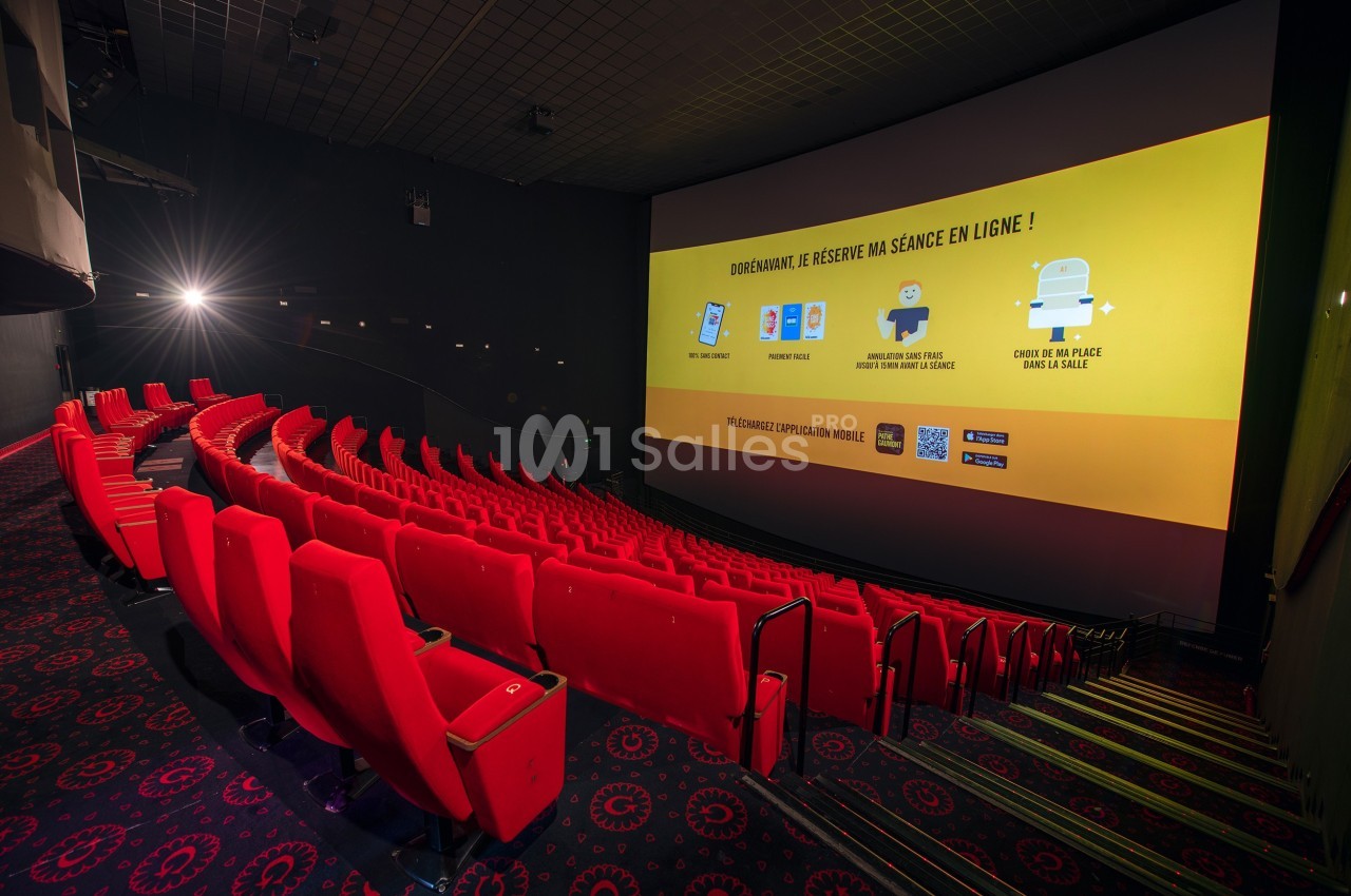 Salle de cinéma vide avec des sièges rouges alignés et un écran affichant des instructions pour réserver en ligne.
