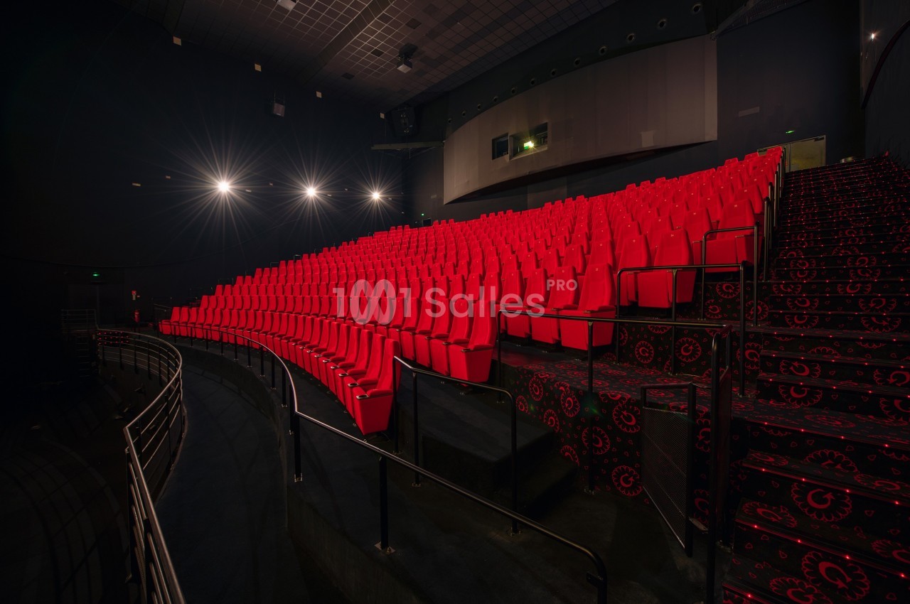 Salle de cinéma vide avec des rangées de sièges rouges et un éclairage tamisé.
