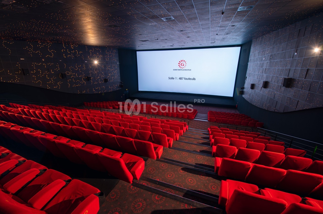 Salle de cinéma vide avec des rangées de fauteuils rouges et un grand écran affichant un logo et un texte.
