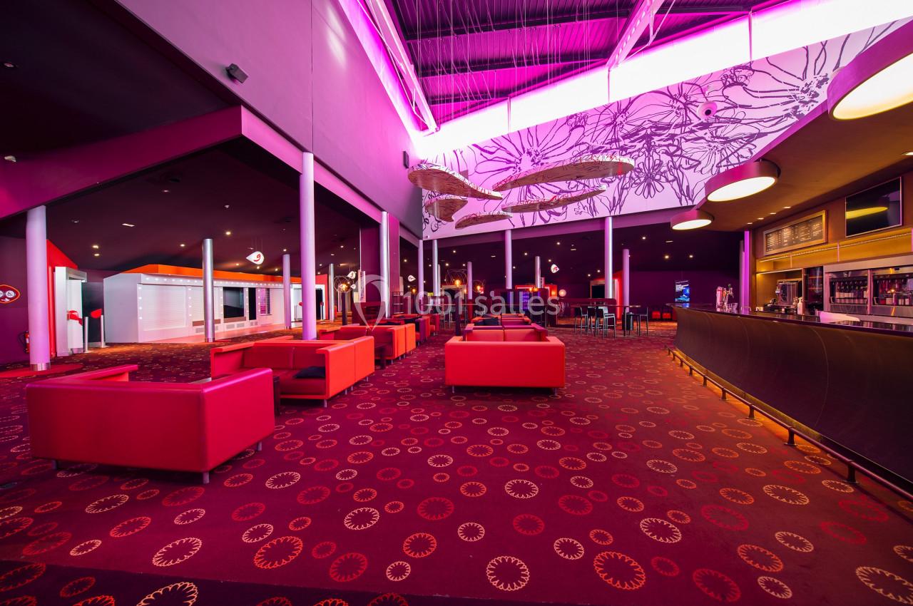 Intérieur d'un espace lounge avec fauteuils rouges, bar à droite et éclairage néon rose au plafond.