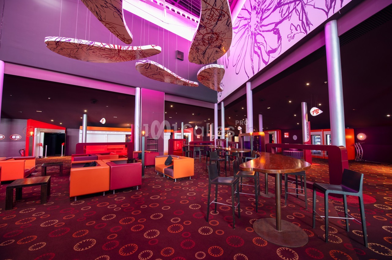Salle moderne avec mobilier coloré, éclairage tamisé et décorations suspendues dans un espace spacieux.