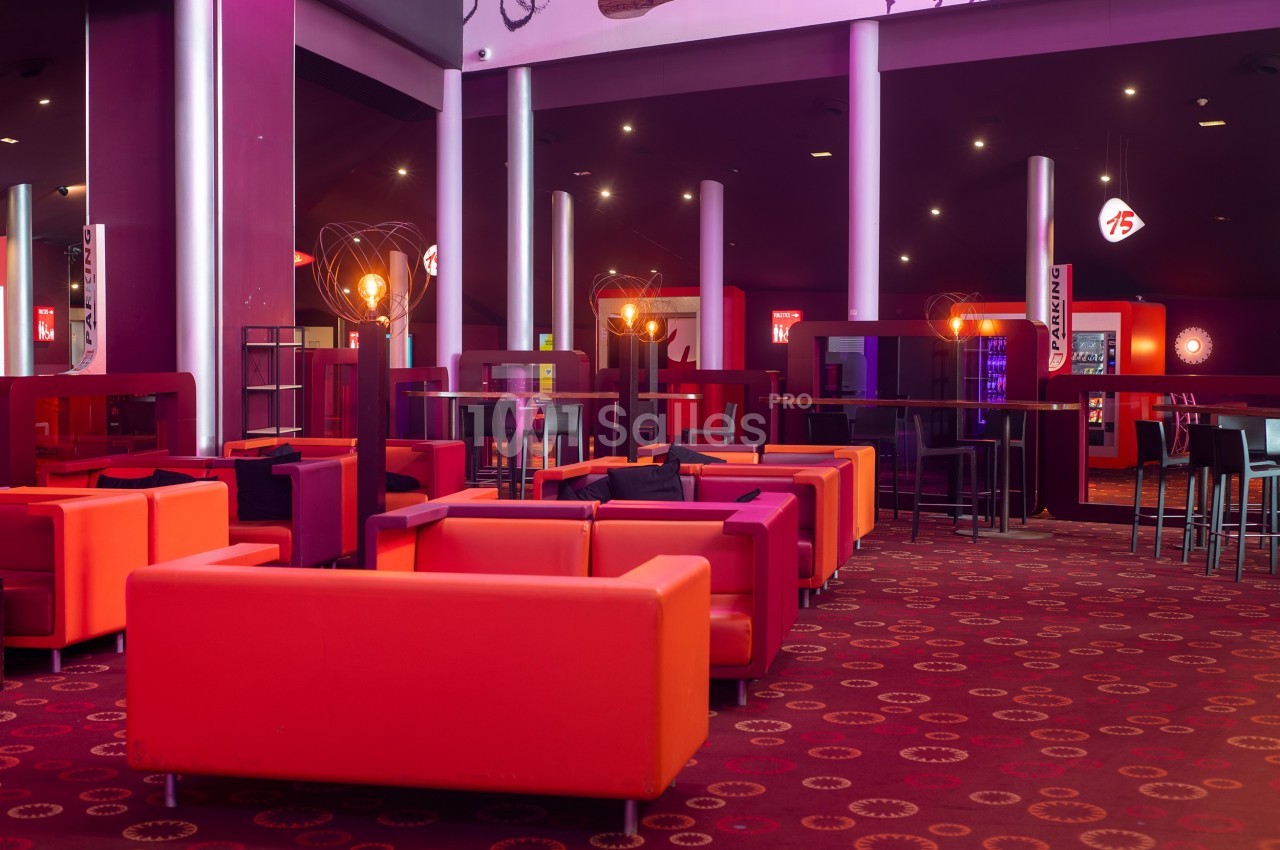 Salle moderne avec fauteuils colorés, tables hautes et éclairage tamisé, dans un espace de détente ou de restauration.